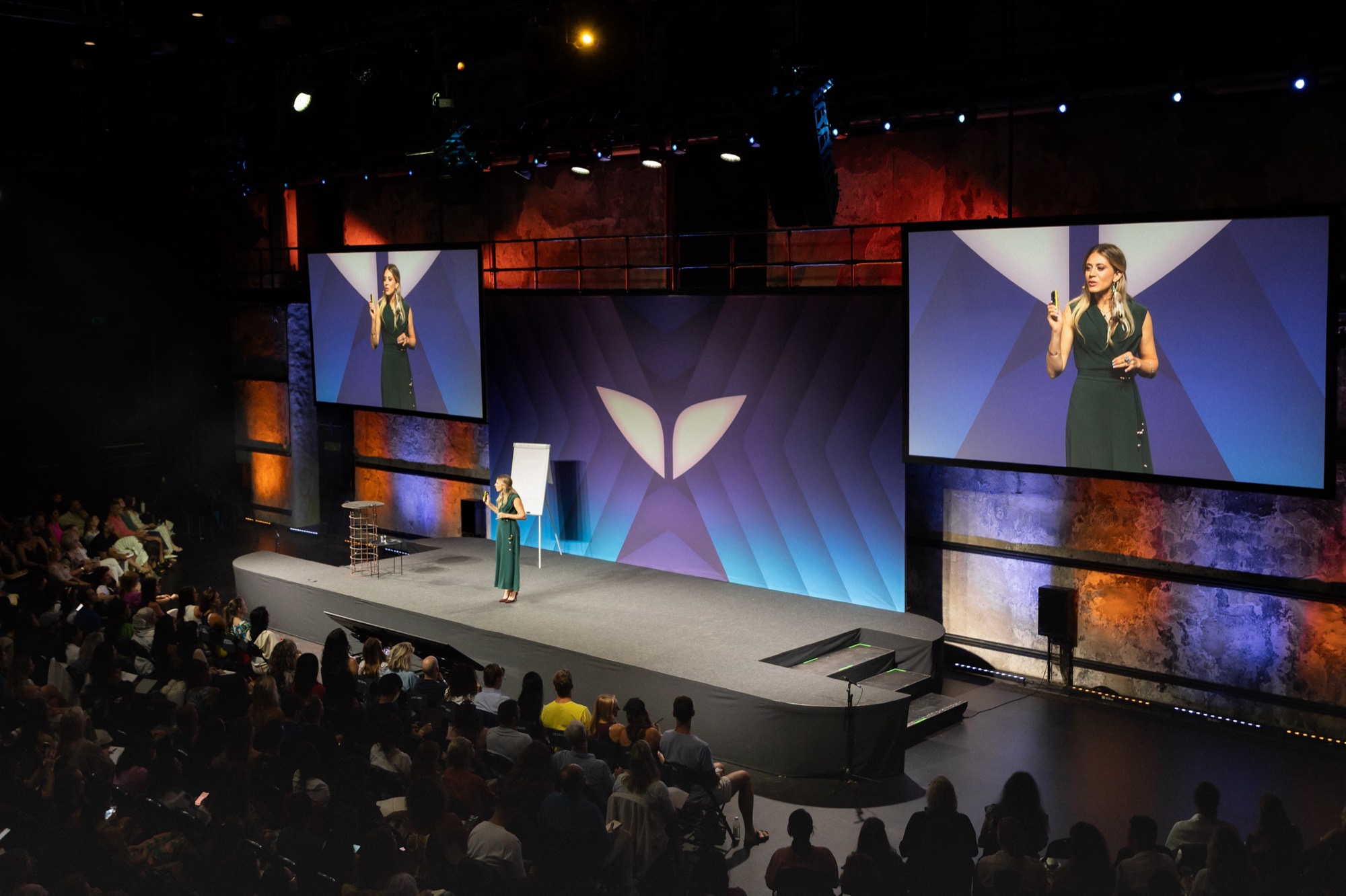 Sabrina Stocker on stage in front of a full auditorium, purple screens behind her